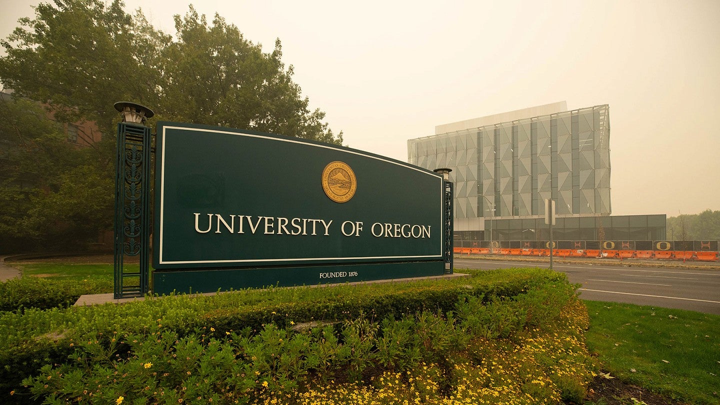 A hazy, tan sky looms over the University of Oregon campus, blurring a deep green University of Oregon sign and a glass building that's under construction.